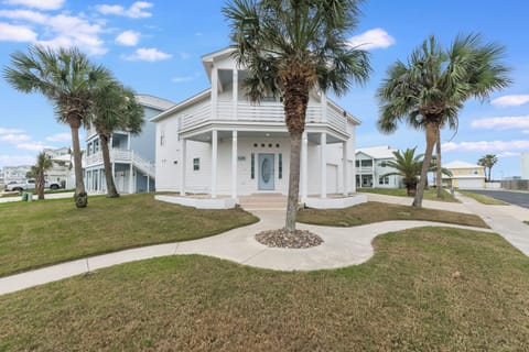 Modern coastal home with elegant white facade, surrounded by swaying palm trees and manicured landscaping in a peaceful residential setting.
