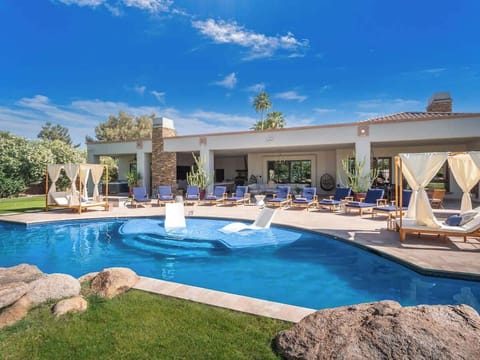 Luxury desert resort features expansive covered patio, designer pool with integrated spa, and lush green lawn under brilliant blue skies—a stunning outdoor retreat.