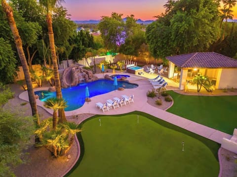 An elevated view captures the property's impressive outdoor area at dusk, featuring a custom pool with waterslide, hot tub, putting green, and mountain views beyond.