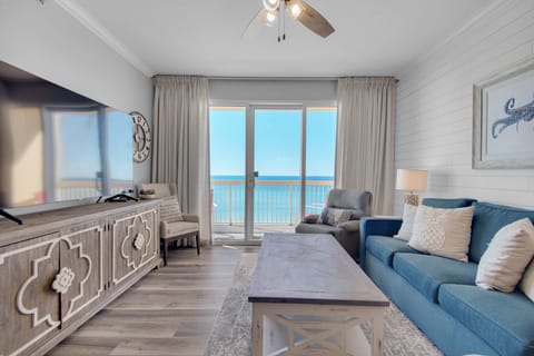 Living Room - Indulge in seaside luxury and comfort with this bright living room, featuring plush furniture including 2 recliners, a large flat-screen TV, and a private balcony over the beach. 