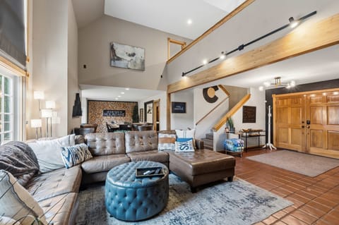 Living room 1: Leather sofa, wood-burning fireplace, large flat-screen TV, and stunning forest views through the expansive windows