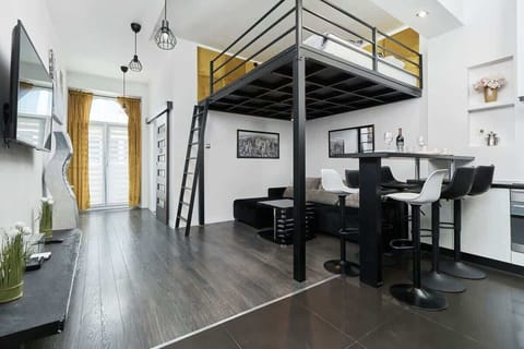 A cozy living room featuring a loft bed above a seating area and dining table, showcasing efficient use of space.