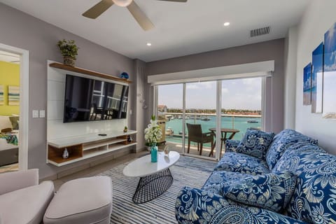 Your living room opens to a private balcony with sweeping turquoise sea views. Sink into the blue patterned sofa, enjoy the cool breeze, and watch boats glide by from your seaside retreat.