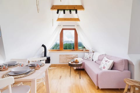 A cozy living area in an attic featuring wooden floors, a comfortable pink sofa, and large windows for natural light.
