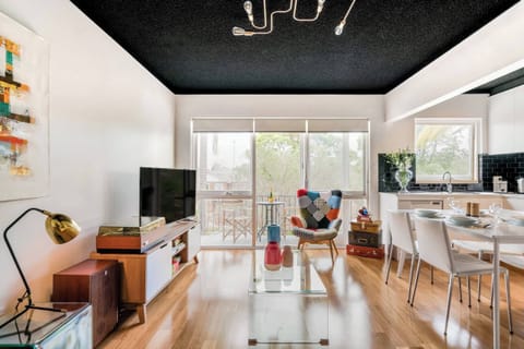 Bright and comfortable lounge area featuring a cosy sofa and TV, with easy access to a private balcony and conveniently located beside the kitchen — perfect for relaxing or entertaining during your stay.