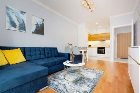 A modern living room featuring a stylish blue sofa with vibrant yellow pillows, complemented by a gray rug and a glass coffee table. Perfectly lit with natural light.