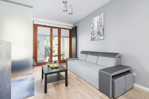A modern living space with a gray sofa, wooden flooring, and natural light from large windows, creating a welcoming ambiance.