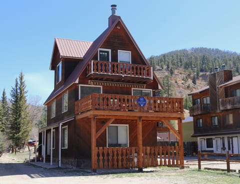 A charming three-story alpine chalet nestled in a forested mountain valley, offering a secluded retreat surrounded by natural beauty and neighboring homes.