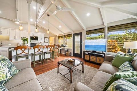 Bright living area with sofa, dining table, and large windows overlooking greenery