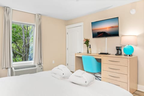 A well-lit bedroom features a wooden desk with a flat-screen TV and a queen-sized bed, creating a cozy and functional space.