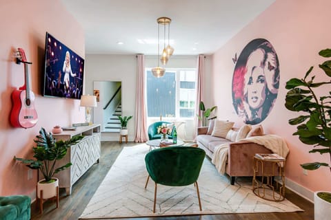 The living room centers on a pink sofa, green chairs, and that iconic Dolly mural, with a staircase connecting all levels of the home