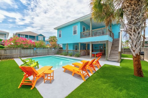 Vibrant turquoise beach house with private pool, colorful lounge chairs, and tropical palm trees creating your perfect coastal retreat.