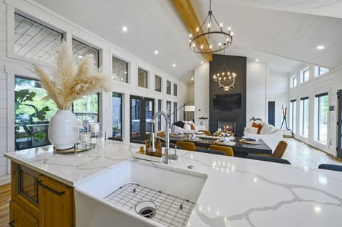 A beautifully designed open-concept dining and living space with vaulted ceilings, modern chandeliers, and large windows that flood the room with natural light and forest views.