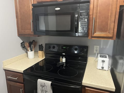 View of kitchen showing stove, microwave, fridge,  toaster, and utensils. 