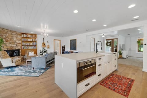 Open‑concept living area with stone fireplace, books, and cozy seating flowing from the kitchen—ideal for families and small groups.