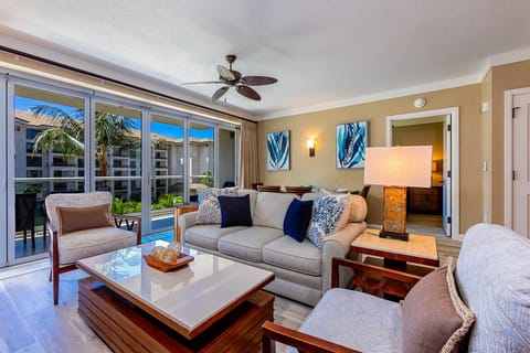 Step into your bright, tropical living room where coastal elegance meets comfort. Relax on plush seating, enjoy the breezy ceiling fan, and step outside to your private patio through sliding glass doors.