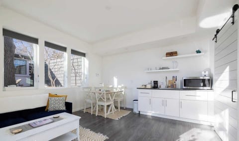 - Sleek white kitchenette stocked with essentials for morning coffee or light bites
- Open shelving and minimal decor keep the space fresh, functional, and inviting
- Dining area with seating for four is ideal for meals, games, or remote work session