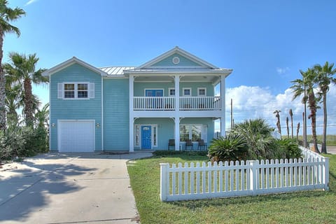 Charming coastal property featuring turquoise siding, white picket fence, and palm trees creating the perfect beach house atmosphere.