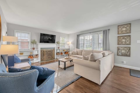 Spacious and stylish living room in our Airbnb with seating for 10 and a large, wall-mounted smart TV. Modern decor, neutral color palette, and ample natural light create a calming atmosphere. Perfect for relaxing after a day of exploring and spending time with loved ones.