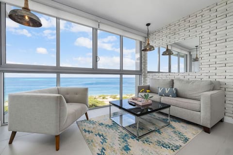 Unwind in your modern living room where floor-to-ceiling windows frame stunning ocean views. Relax on plush seating and soak in the coastal ambiance with industrial-chic lighting overhead.