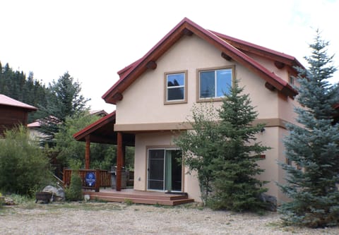 Charming mountain home with red roof and welcoming covered porch, nestled among evergreens in a peaceful forested setting.