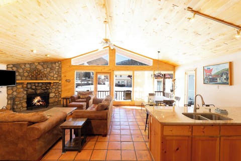 Relax in your spacious living area with a crackling stone fireplace, vaulted pine ceilings, and mountain views through expansive windows. The open layout connects you to a fully equipped kitchen and dining space.