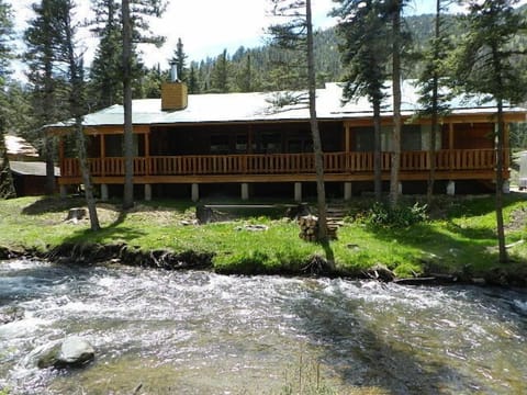 Mountain lodge nestled beside a rushing creek, surrounded by towering pines and forested slopes, offering a peaceful retreat in a scenic natural setting.