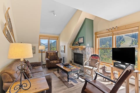 Cozy up by your stone fireplace with stunning mountain views through large windows in this warm, inviting living space.