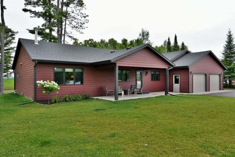 A modern, red-sided vacation home with black trim, a gray roof, and an attached two-car garage, situated on a green lawn.