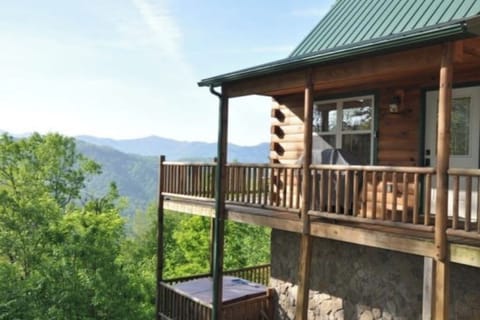 Covered upper-level deck with log railings overlooking the Smoky Mountain landscape near Bryson City. A private hot tub is visible beneath the deck.