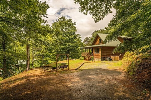 Front approach to the cabin with a wooded driveway and covered porch surrounded by mature trees. This secluded Bryson City cabin setting highlights easy access and a private Smoky Mountains atmosphere.