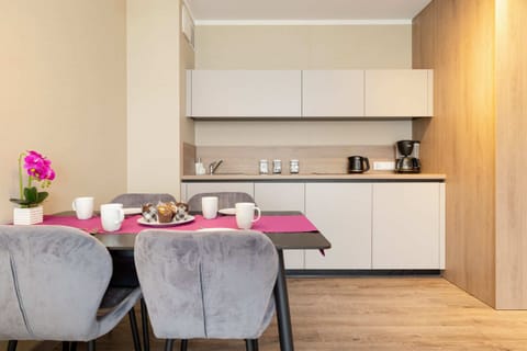 A fully equipped modern kitchenette with white cabinetry, alongside a dining table with upholstered chairs.