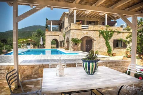 View of the pool and main villa from the outdoor seating area, showing the stone exterior and surrounding landscape.