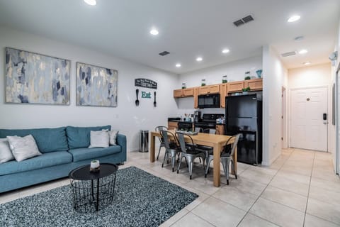Relax in the bright open-concept living area featuring a cozy blue sofa and chic circular coffee table. The stylish dining set is perfect for meals, enhanced by modern artwork that adds a touch of flair to the space.