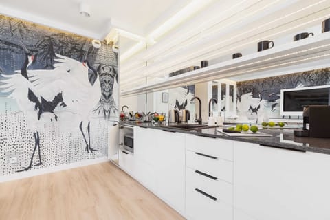 A sleek kitchen with white cabinets, integrated appliances, and wooden flooring, opening to the living space.