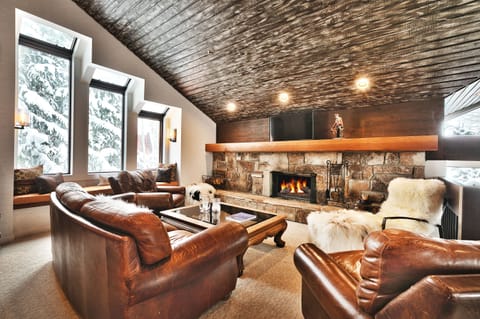 Comfortable seating in leather couch and armchair, mantle mounted smart TV over the wood burning fireplace