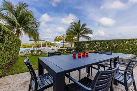 Waterfront dining setup framed by lush palms and tropical greenery, with pool, cabanas, and serene turquoise waters as a picturesque backdrop.