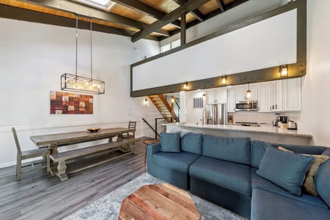 Soaring ceilings and exposed beams create an airy loft-style space where you can unwind on the plush sectional, share meals at the rustic dining table, and enjoy the open-concept design.