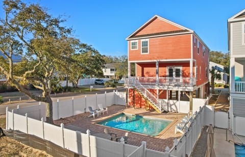 Charming coral beach house with private pool surrounded by white fencing in a peaceful residential neighborhood.