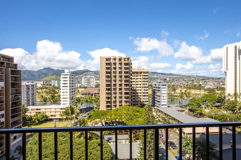 Urban Honolulu spreads beneath a brilliant sky, with lush greenery framing residential towers and mountain ridges defining the horizon.