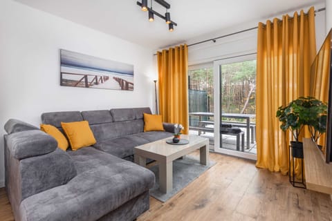 A cozy living room with a gray sofa, yellow curtains, and a modern TV. A small plant adds a touch of greenery, creating a warm and inviting space.