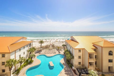 Beachfront resort complex featuring multiple buildings with terracotta roofs, swimming pool, and direct beach access under blue skies.