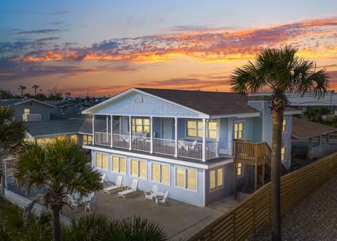 This coastal property showcases a stunning two-story beach house with expansive balconies surrounded by swaying palm trees during golden hour.