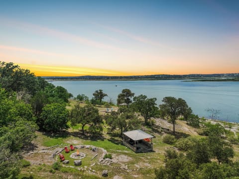 Aerial view of waterfront property with lakeside setting, fire pit area, and private pavilion, right on the water's edge.