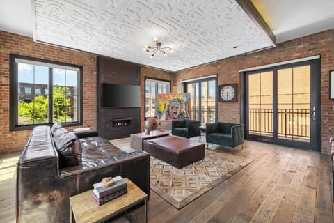 Spacious open-concept living area featuring exposed brick walls, comfortable lounge seating, a Smart TV, stylish décor, a vintage record player and record collection, plus direct access to a private balcony.
