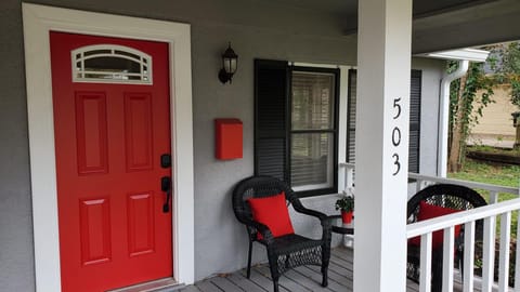Two wicker chairs and a table on one end of the front porch