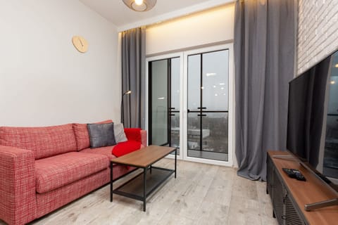 Bright and cozy living space featuring a vibrant red sofa, large windows, and a TV unit. Ideal for relaxation and entertainment.