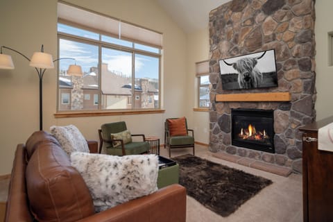 Cozy up by your stone fireplace with mountain views through expansive windows in this inviting living space.