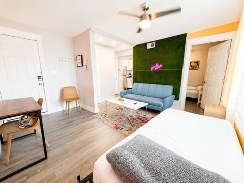 Experience our vibrant living room, featuring a blue couch, pastel pink chairs, and a big TV. Minimalist decor, ample natural light, and modern furnishings create a bright, airy, and inviting space for relaxation and socializing.