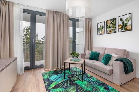 A cozy living room with a green color palette, modern furniture, and large windows letting in natural light.
